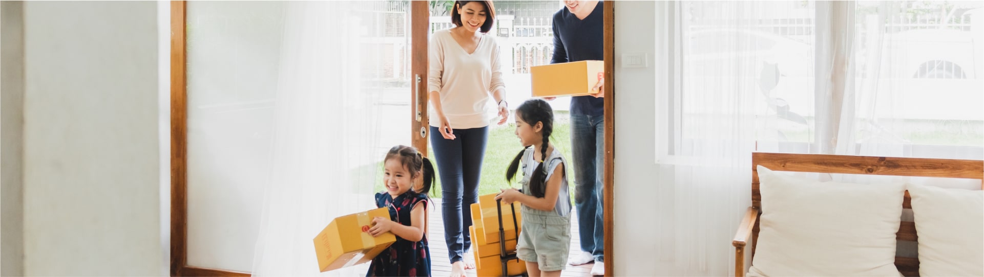 Family of four entering a house, carrying boxes.