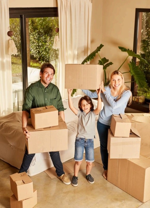 Family of three holding cardboard boxes in a new home.