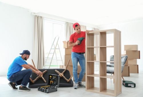 Two men assembling furniture in a room with boxes and tools.