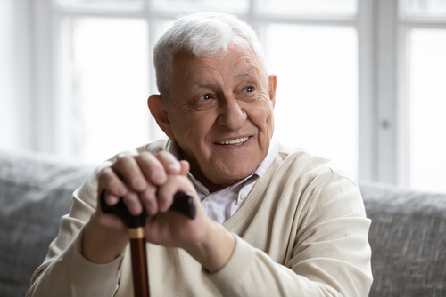 An elderly man with a cane smiles at the camera.