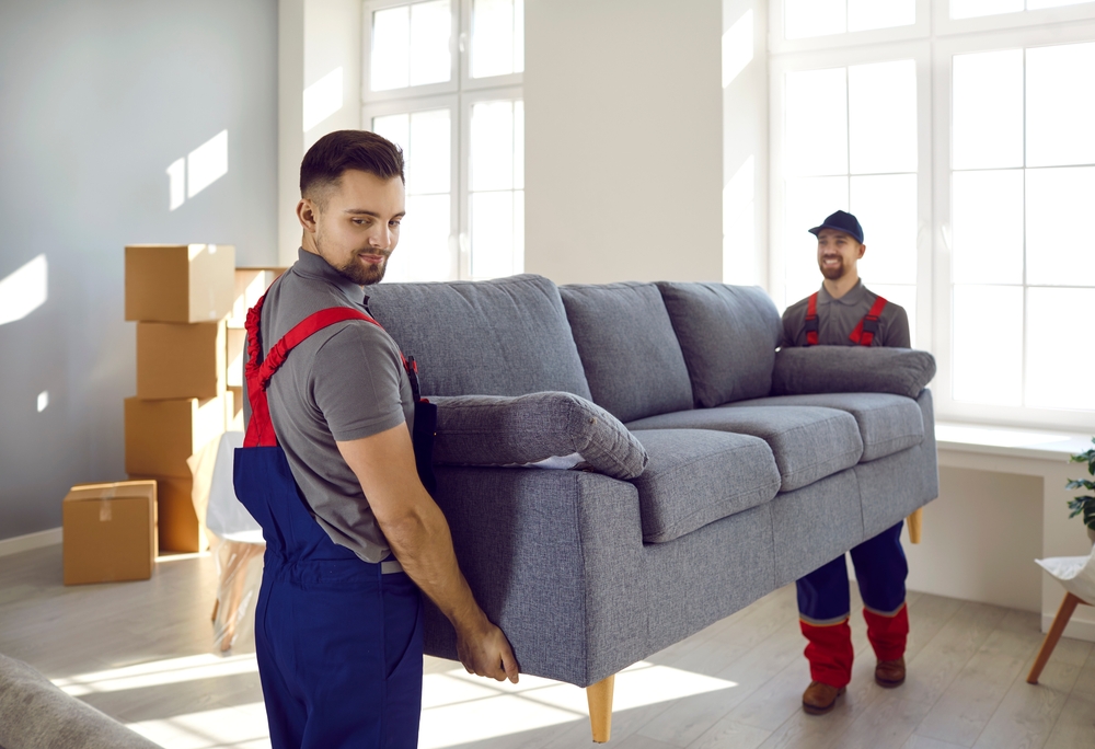 Two men in matching uniforms carrying a gray couch.