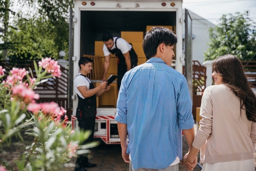 Couple watching movers unload boxes from a truck.