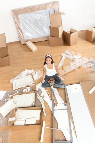 Woman sitting on the floor surrounded by furniture parts and boxes.